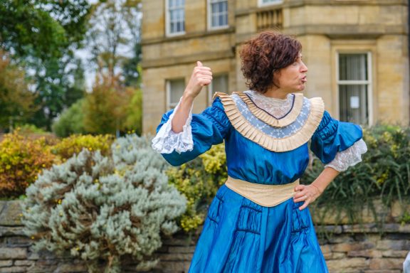 A woman in a blue vintage dress striking a pose in a garden setting.